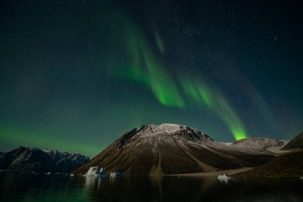 Photo of The aurora borealis (northern lights) shows its colors in a protected bay on a calm night over a snow-dusted mountaintop