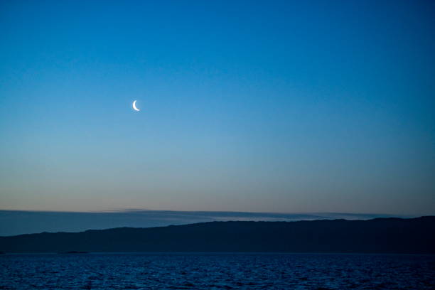 istock A sicle moon rises over clouds, a low ridge and the sea 1324913017