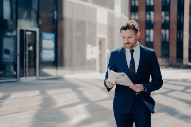 istock Successful businessman in formal wear reads newspaper while walking 1324918196
