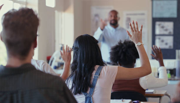 scatto di retrovisore di studenti che alzano la mano durante una lezione con un insegnante in classe - educazione secondaria di scuola media foto e immagini stock