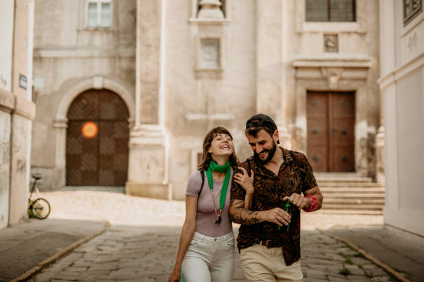 Cute and spontaneous young adult couple, being colorfully dressed, walking down the small street, interlaced hands and enjoying the beer and talk. Loving traveling and music festivals
