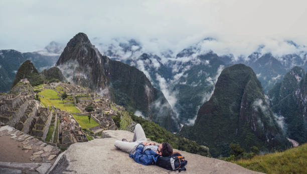 Young man laying down contemplating Machu Picchu Panoramic shot of young man laying down, contemplating Machu Picchu lost city with Huayna Picchu. Ruins of ancient inca civilization in the sacred valley of Cusco Province. Peru, South America machu picchu photos stock pictures, royalty-free photos & images