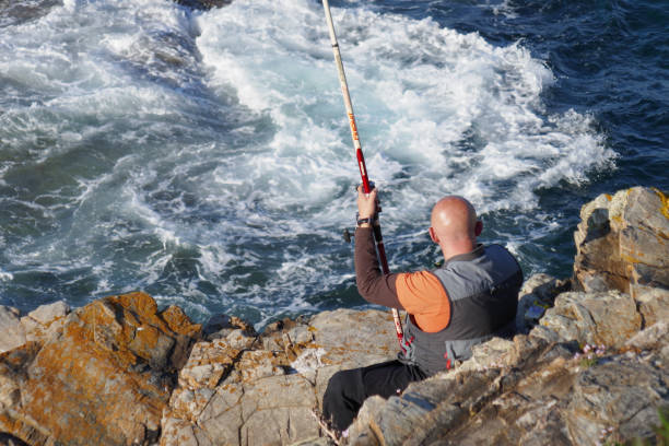 Bald man fishing with fishing pole rod from cliffs rocks stock photo