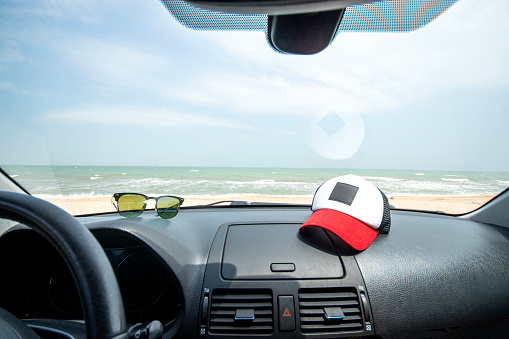 Sea view through the car windshield. Travelling by car to the sea. Cap and sunglasses lie on the car dashboard.