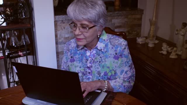 A Senior Latin American Lady Works From Home On Her Laptop Computer Sitting At Her Dining Table