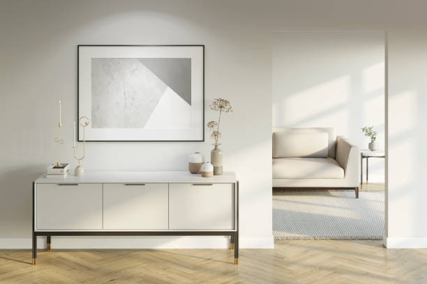 istock Modern white interior with an illuminated horizontal poster above a light-colored cabinet with decor, a doorway to a room with a sofa, and a coffee table with a parquet floor. Front view. 1324932122