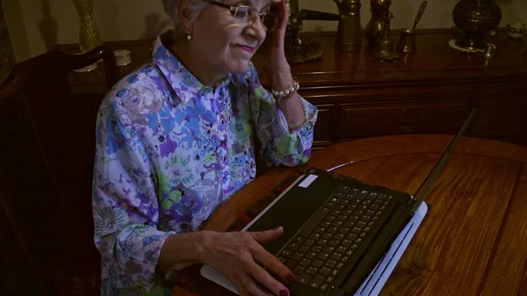 A Senior Latin American Lady Works From Home On Her Laptop Computer Sitting At Her Dining Table