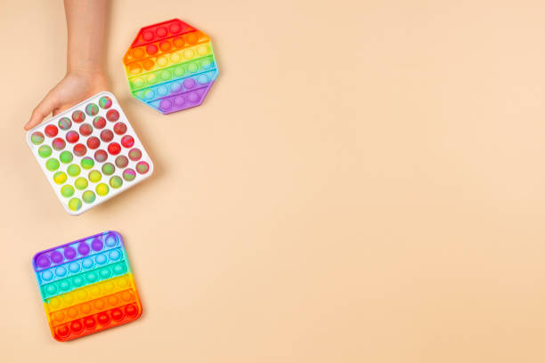 istock Kid hand holding pop it fidget toy on pastel background. Push pop-it fidgeting game helps relieve stress, anxiety, provide sensory and tactile experience for children 1324939132