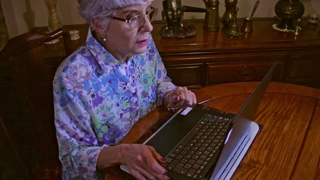 A Senior Latin American Lady Works From Home On Her Laptop Computer Sitting At Her Dining Table