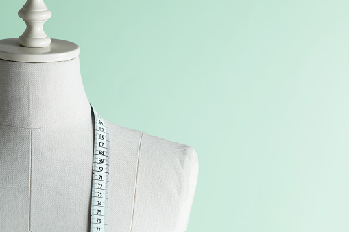 Tailor Mannequin with measure tape in front of green background.