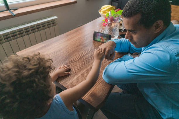 istock Father with son sitting at dining table. Boy watching cartoons on smartphone 1324939767