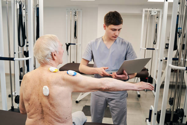 istock Physical therapist with laptop conducting back muscles diagnostics for retiree 1324940382