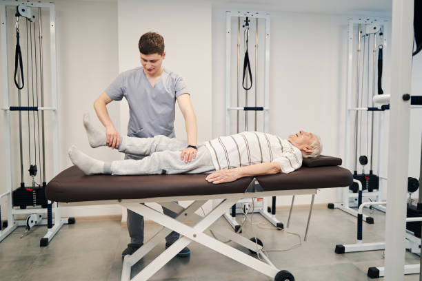 istock Physical therapist pulling old male right leg during treatment activity 1324940519