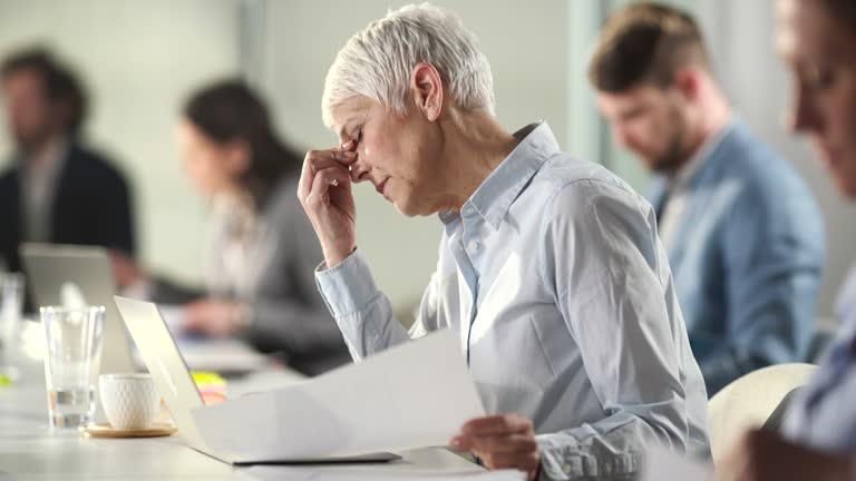 Tired senior businesswoman having headache after seeing bad business report.