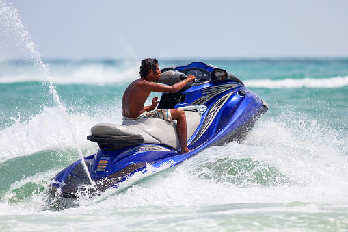 Koh Samui, Thailand - January 2, 2011: San-tanned man running a jet-ski in the sea waves of Chaweng beach of the Samui Island
