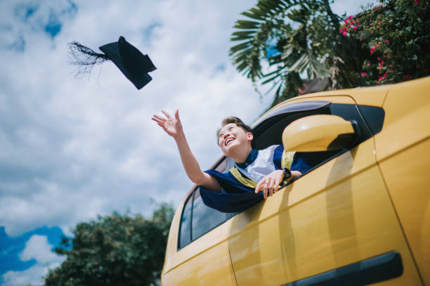 asian chinese young female with graduation gown throwing mortarboard cap in the air from driver seat of her car laughing - university graduation car student imagens e fotografias de stock