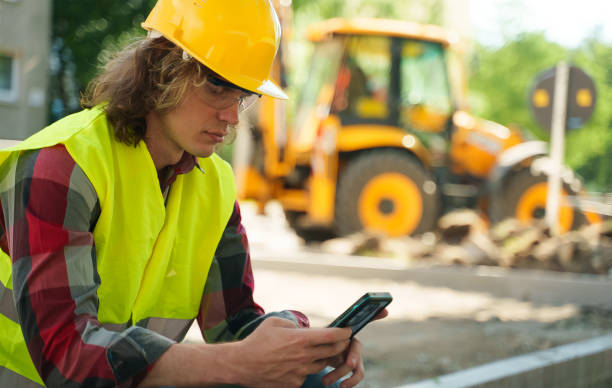 istock Male worker in hardhat and high vis jacket using smartphone. 1324944092