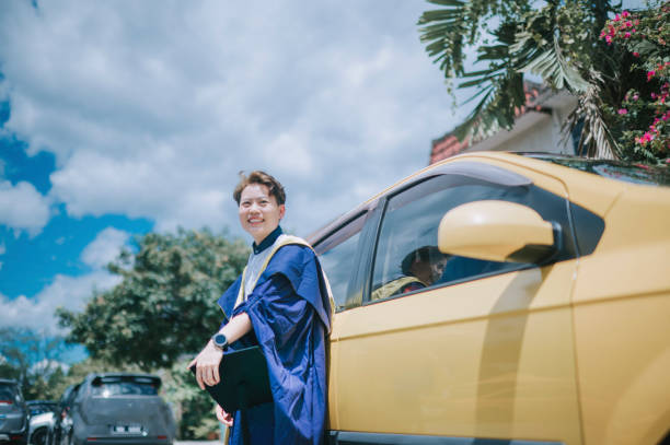 asian chinese young female with graduation gown leaning on her car looking at camera smiling - university graduation car student imagens e fotografias de stock