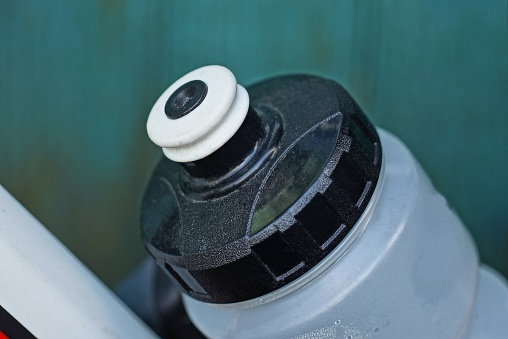 part of a white plastic water bottle closed by a black cap on a bicycle on a green background