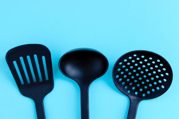 istock Kitchen utensils for cooking. Black plastic ladle, spatula and ladle on turquoise background. 1324945426