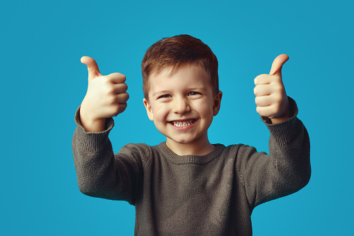 A laughing little boy holds his thumbs up against the white background