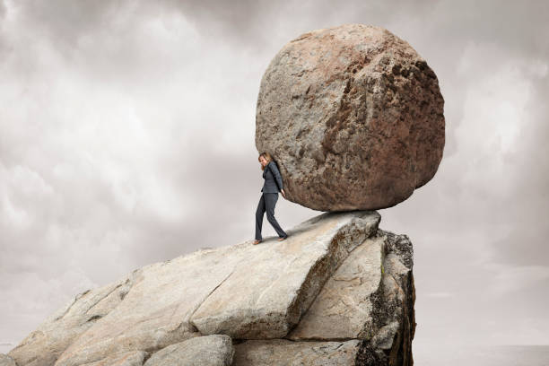 Woman Pushes Large Boulder Off A Cliff A businesswoman attempts to push a giant round boulder off of a cliff.  The monochrome background and ky provide ample negative space for copy and text. boulder rock photos stock pictures, royalty-free photos & images