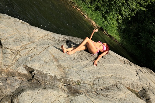 A woman lying on a rock sunbathing. She is wearing a pink bikini.