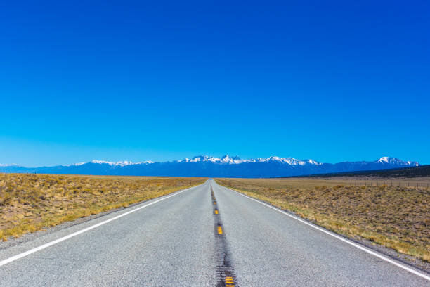 istock Colorado Road Trip: Sunny Road Ending in SnowCapped Mountains 1324957846