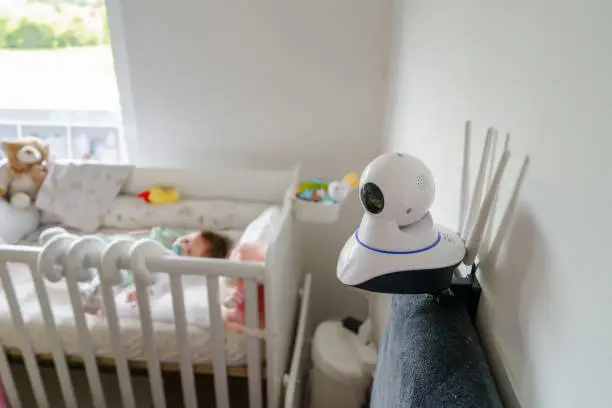 Surveillance security camera on the bed at home in bedroom watching small child baby in cradle while sleeping