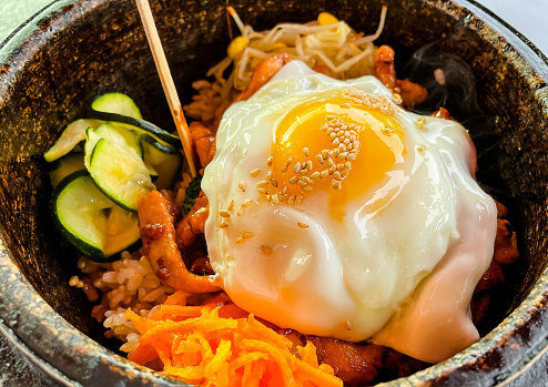 Close up view of authentic korean hotstone bowl with sunshine egg, chicken, bean sprouts, carrots, and cucumbers
