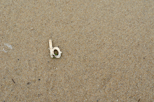 The letter B on the wet yellow sand. The white plastic letter is carried out on the sandy beach by a wave. View from above. Copy space.