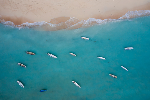 Aerial drone landscape in bird eye mode of numerous wooden boats anchored in turquoise waters of a white sand beach in Nusa Lembongan in Bali Indonesia.