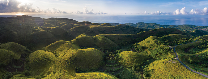 Aerial drone panoramic view at sunrise of the lush hilltops and valleys with scenic sea views and located on the island of Nusa Penida in Bali in Indonesia.