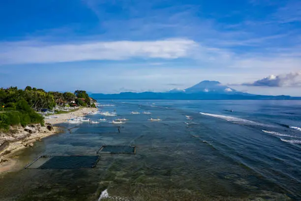 Aerial drone view of Nusa Penida coastline with the mighty volcano Agung spotted on mainland of Bali.