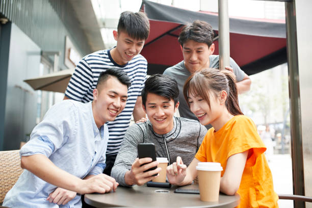 adultos jóvenes asiáticos mirando el teléfono celular juntos en una cafetería al aire libre - mobile phone coffee shop group of people women fotografías e imágenes de stock