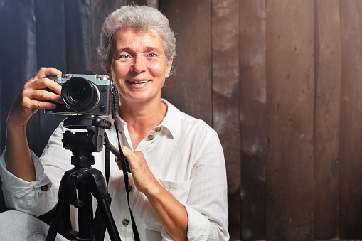 Portrait of elderly woman photographer with camera on wooden background