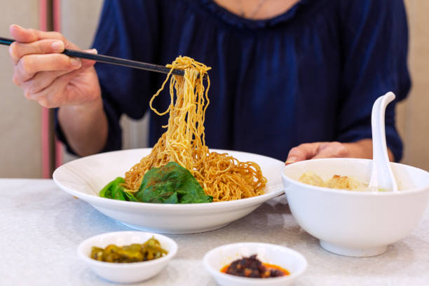 woman using chopsticks to eat noodles from plate