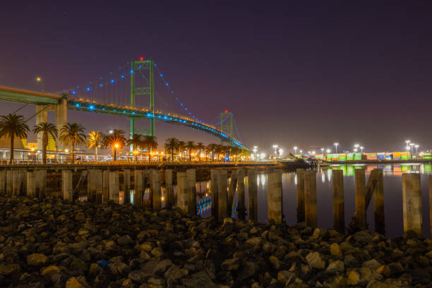 Vincent Thomas Bridge in Long Beach CA with the pier and the San Pedro shipping yard San Pedro, California - USA: The Vincent Thomas Bridge is located in San Pedro and the Long Beach area with many shipping containers and construction equipment for repairs and shipping services with some smaller boats and a yacht and on this day it looks like a very busy facility under and around this very high and large bridge for the larger ships. san pedro los angeles photos stock pictures, royalty-free photos & images