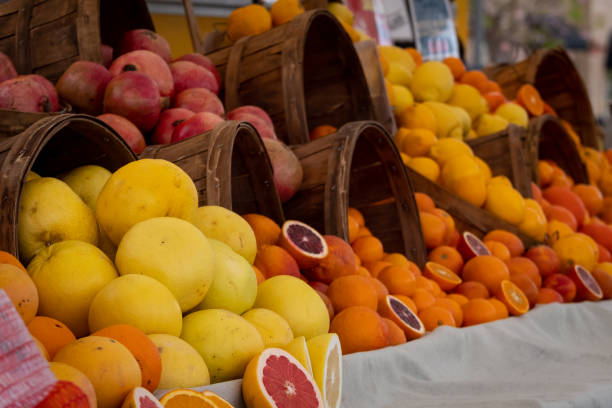 A display of lemons, grapefruit, pomegranates, and oranges displayed in wooden barrels on a table. The warm colors of red, yellow, and orange pair beautifully with the brown wood of the barrels creating an excellent color pallet for a background image.
