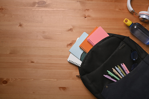 Backpack with school supplies on wooden background. Back to school concept.