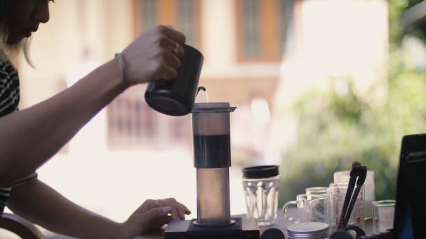 Young Asian woman preparing to make coffee at home. She pouring Hot water being over roasted coffee beans and dripping through a filter. , drip coffee In morning, coffee time. , enjoying relaxation.,looking happy,lifestyle concept