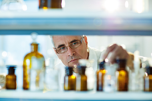 Senior scientist choosing the right bottle from a shelf while working on his research in laboratory.