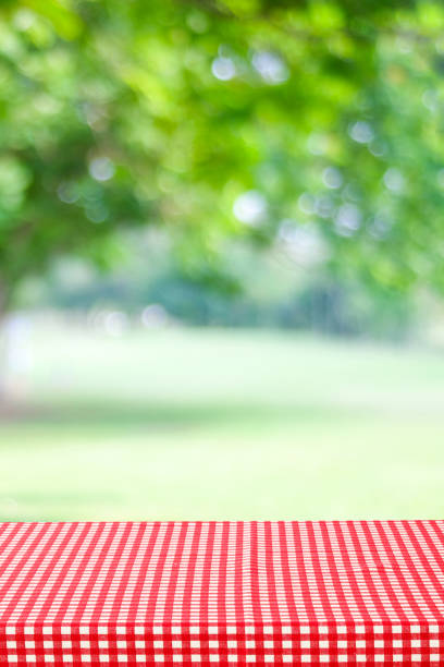 istock Empty table with red and white tablecloth over blurred park nature background, for product display montage, spring and summer 1324996597