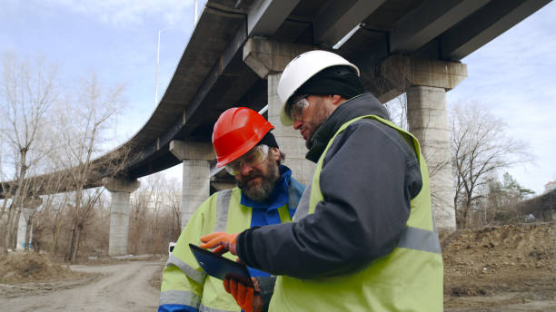 Male builders with tablet discussing data in outskirts Mature and adult man using tablet and talking while standing near concrete bridge in outskirts real time stock pictures, royalty-free photos & images