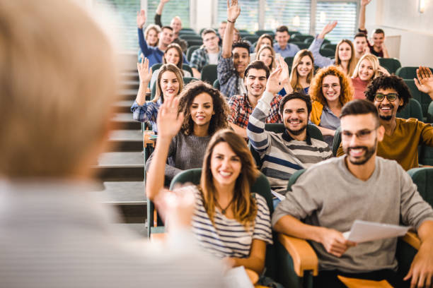 istock Happy college students raising their hands on a class at lecture hall. 1324996640