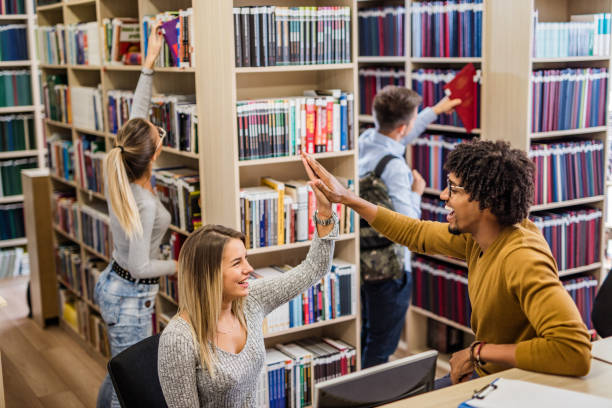 Happy university students giving each other high-five in library.