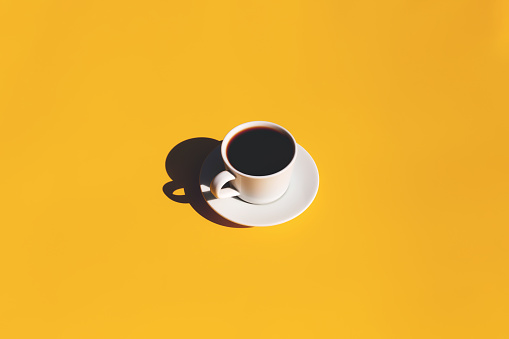 Single white cup and saucer plate of black espresso coffee from top view with shadow of sun on yellow terracotta background. High quality photo