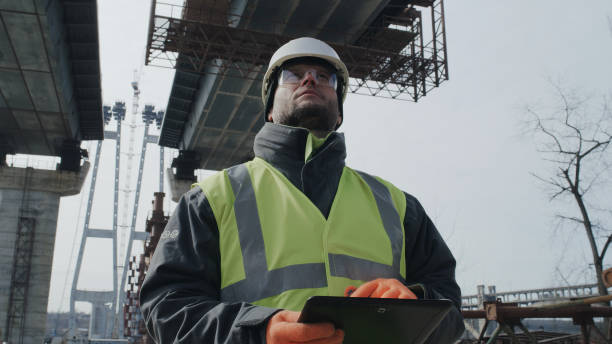 Man using tablet on bridge construction site Male builder browsing data on tablet while standing under unfinished bridge during work on construction site real time stock pictures, royalty-free photos & images