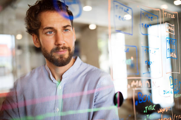 istock Handsome man working and writing on glass board in office. Business, technology, research concept 1324998944