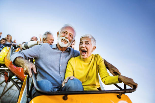 happy senior couple having fun while riding on rollercoaster at amusement park. - lunapark treni stok fotoğraflar ve resimler